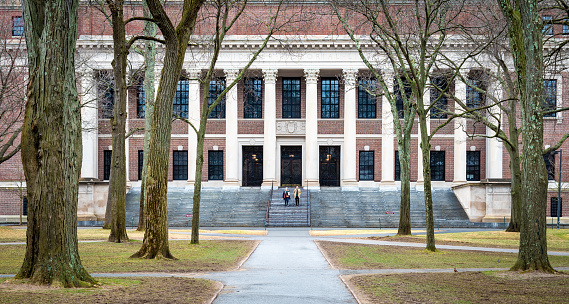 Cambridge, MA, USA - March 20, 2024: view of the iconic architecture of the famous Harvard University in Cambridge, Massachusetts, USA on a winter day with some locals and students passing by.