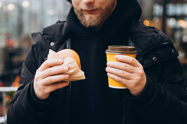 istock Bearded man with a burger and a cup of coffee outside on a blurred background. 2106776438