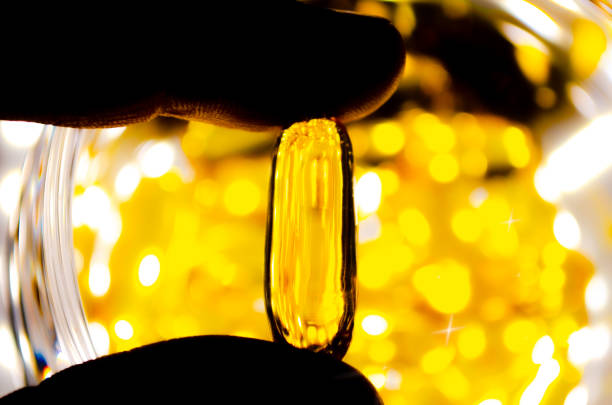 Fingers holds yellow medication capsules of omega 3 A E  fish oil healthy supplement pills Biological supplements Top view Diet fat-soluble vitamins Golden vitamin D3 shining background Magic pill