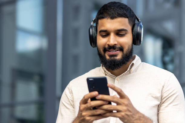 istock Smiling young man enjoying music on headphones while using smartphone outdoors 2106836257