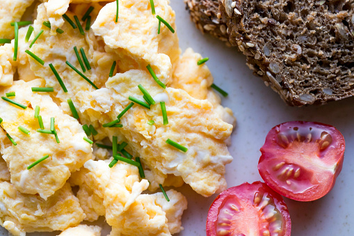 Scrambled eggs with tomatoe, dark bread and chives, ready-to-eat on a plate, close-up