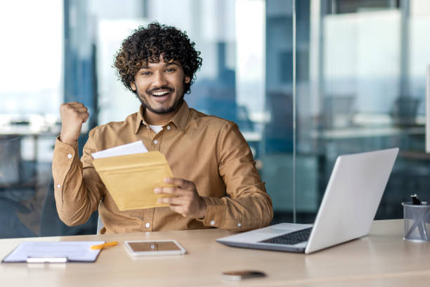 istock Rejoiced middle eastern male holding opened envelope and making winner gesture with hand in corporate building. Happy bearded businessman receiving mail letter with pleasant bank notification 2106838705