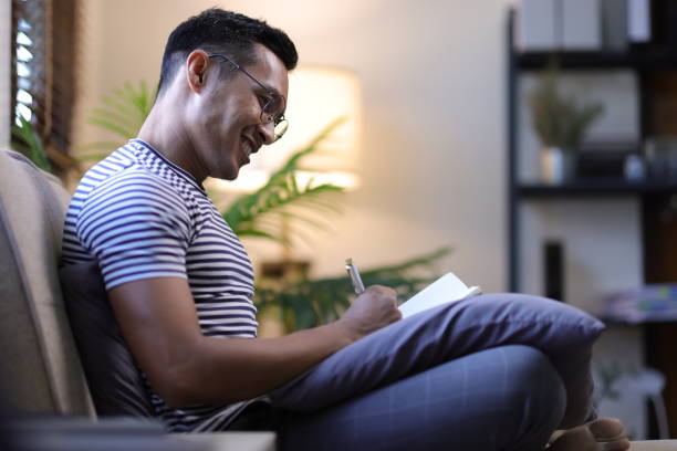 istock Man reading a book and writing a diary while relaxing on the sofa at home. 2106878817