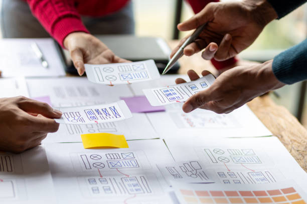 istock UX, UI designers collaborate to design user interfaces for smartphone apps based on user experience. Colleagues meeting, program designers brainstorm to discuss designing mobile applications. 2106881522