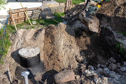 Using an excavator to bury a 10 m3 concrete septic tank located in the garden next to the house.