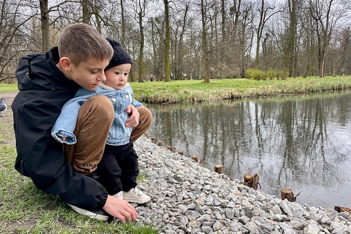 A teenager with a baby brother are watching birds by the river in early spring.