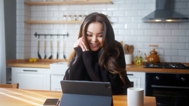 istock Smiling young asian woman sit in the kitchen having video call conversation through tablet computer. Share news, talk to family, enjoy webchat virtual meeting 2106910767