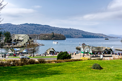 View across lake Windermere in the UK.  Pleasure boats can be seen moored and people can be seen on the promenade