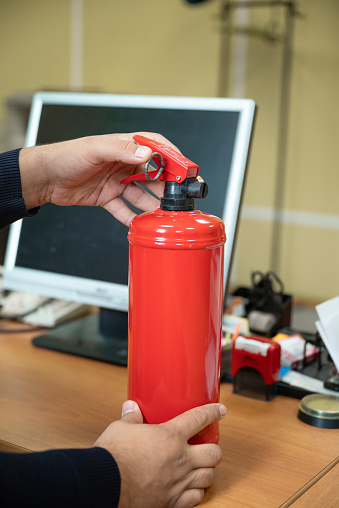 man holds a fire extinguisher in his hands against the background of office equipment. The concept of fire safety