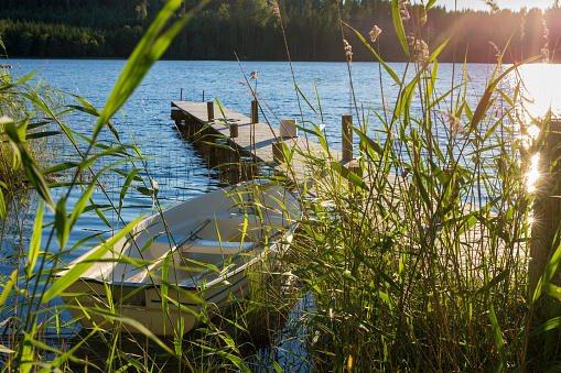 Rowboat is moored at a wooden jetty in a green area in a Swedish lake in the evening sun