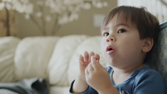 Asian two-year-old baby eats grapes and watches TV attentively.