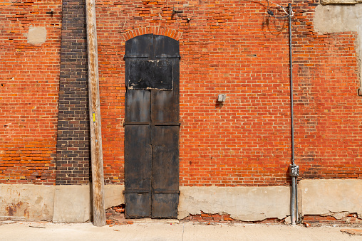 Brick wall and old metal door in sun lit alley.