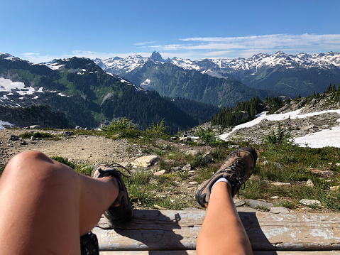 View past hiker's legs relaxing on viewpoint above mountains