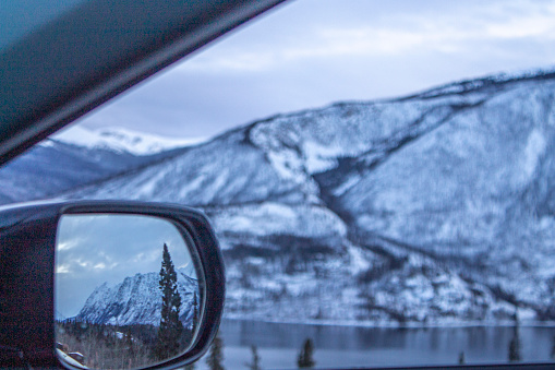 Concept of travelling by car. Beautiful winter landscape in side mirror