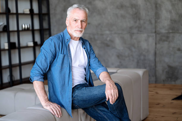 istock Middle aged man in denim shirt sitting on sofa and looking at camera 2106986951
