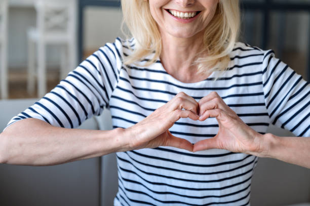 istock Smiling mid aged woman making heart hand gesture sign 2106987487