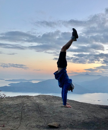 Young man performs handstand on mountain top above ocean and islands