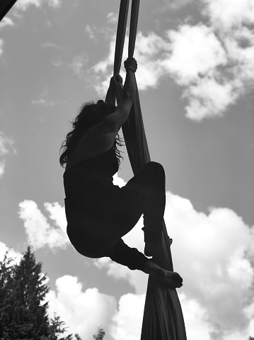 Young woman climbs ropes into sky with lofty clouds