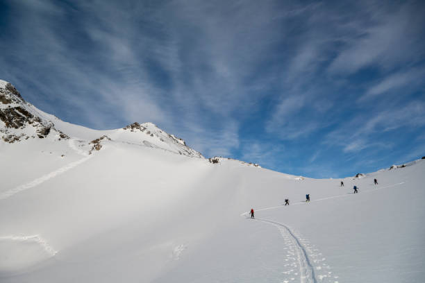 Distant view of ski mountaineers ascending snowcapped mountain above glacial plain