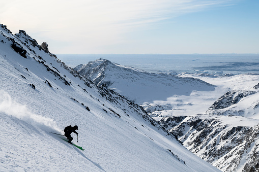 Distant view of ski mountaineer descending mountain in fresh powder snow above glacial plain