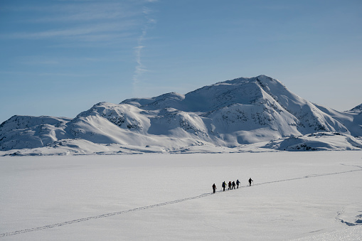 Distant view of ski mountaineers ascending snowcapped mountain across glacial plain