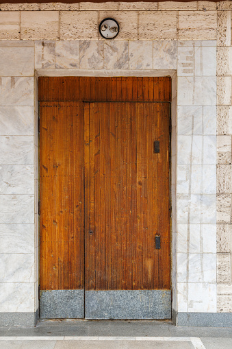 old wooden door of soviet public building in a wall made of shell rock and marble, bottom of the door is covered with zinc plated steel sheets