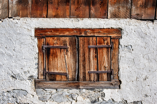 Traditional wooden window shutters of an old farm house in Switzerland. Rusty fittings, weathered plaster wall of barn building.