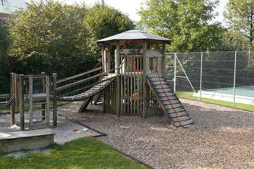 Playground for children made of wood an ropes. It is dominated by a small stilt house with various climbing equipment such as ladder or a bridge. On the ground there is mulch for safety reasons.