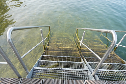 Steel stairs with railings for waterfront access. They lead to water. Front high angle view showing lower part of the steps already in water. There is copy space on the background.