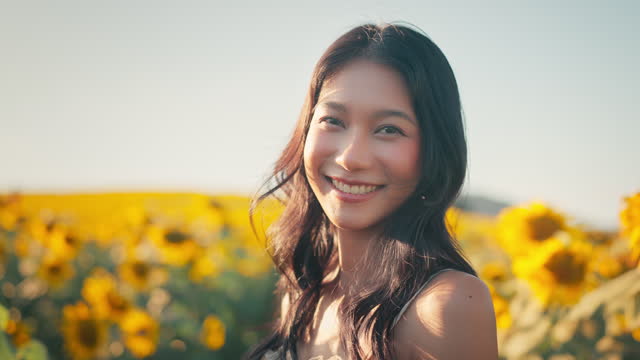 Happy asian woman smiling in sunflower field outdoors, Cheerful Young female looking at the camera feeling free in blooming garden in summer day.