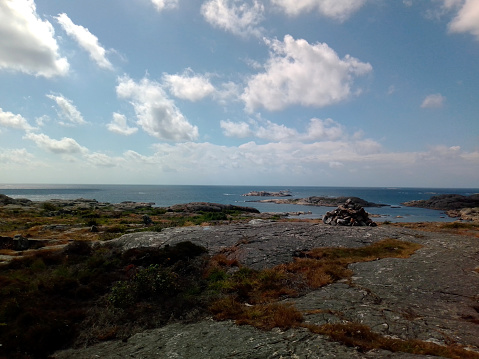 View over the ocean from a rocky shoreline in the summer, blue sky and clouds