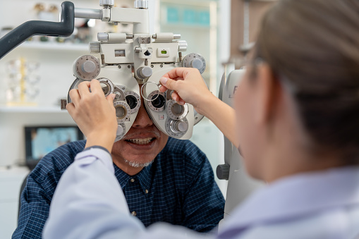 Optometrist adjusting phoropter during eye examination. Professional vision test at optometry clinic. Selective focus with patient in optometrist equipment