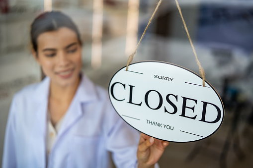 Optical shop owner displaying closed sign. End of business hours at optical retail concept.
