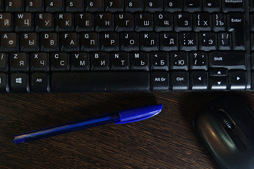 Black keyboard and mouse with blue ballpoint pen lying on dark table