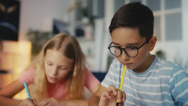 Boy in eyeglasses and his female friend working on a school project at home