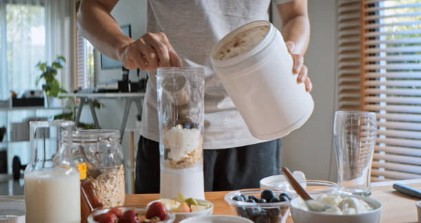 young adult asian man prepare and make protein shake drink, mixed fruit cereal juice, using blender mixer. fitness dietary activity, healthy diet lifestyle, health care nutrition concept - protein bildbanksfoton och bilder