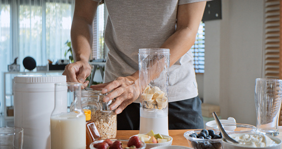 Young adult Asian man prepare and make protein shake drink, mixed fruit cereal juice, using blender mixer. Fitness dietary activity, healthy diet lifestyle, health care nutrition concept
