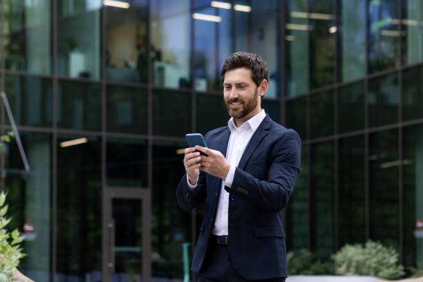 istock Smiling businessman using smartphone in front of office building with confidence 2107391093