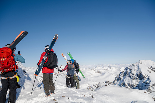Ski mountaineers pause on summit above mountains and glaciers and prepare to descend slope