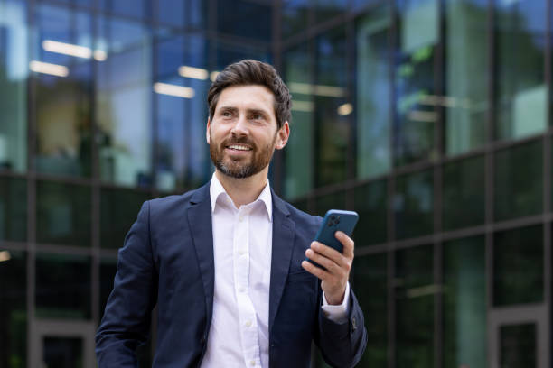 istock Confident businessman smiling with smartphone outside modern office building 2107395880
