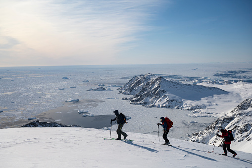 Distant view of ski mountaineers ascending snowcapped mountain across glacial plain