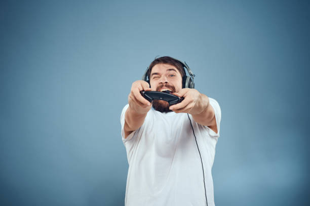 istock Man in headphones controller in hands playing game console lifestyle emotions blue background white t-shirt 2107403945