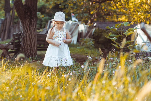 Little girl in white dress and white har looking at something out in the nature