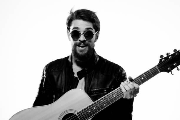 A man holds a guitar in his hands music emotions black leather jacket dark glasses studio light background. High quality photo