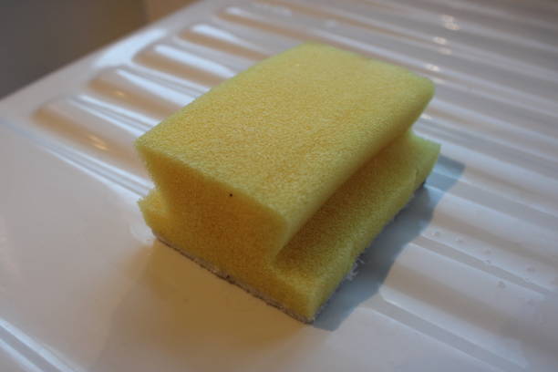 istock Yellow dish washer sponge sitting on a ceramic kitchen draining board 2107457414