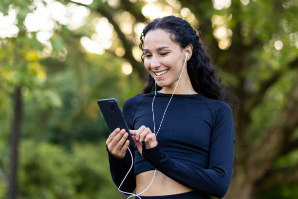 istock Smiling athletic woman with earphones using smartphone in a park setting 2107461896