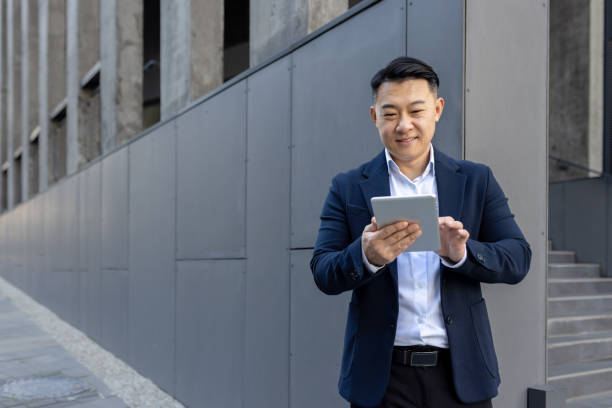 istock Confident asian businessman using tablet outside modern office building 2107469008
