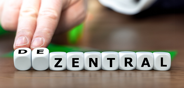 Hand turn dice and changes the German word 'zentral' (centralized) to 'dezentral' (decentralized).
