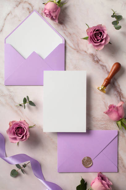 istock Blank wedding invitation card mockup with space for text, violet envelopes, ribbon, roses flowers on marble background. Flat lay, top view. 2107493842
