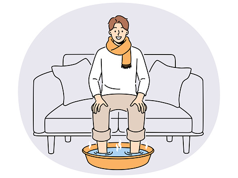 Smiling man in scarf sit on sofa at home soak feet in hot water. Happy male suffer from cold or flu do procedures for fast recovery. Healthcare. Vector illustration.